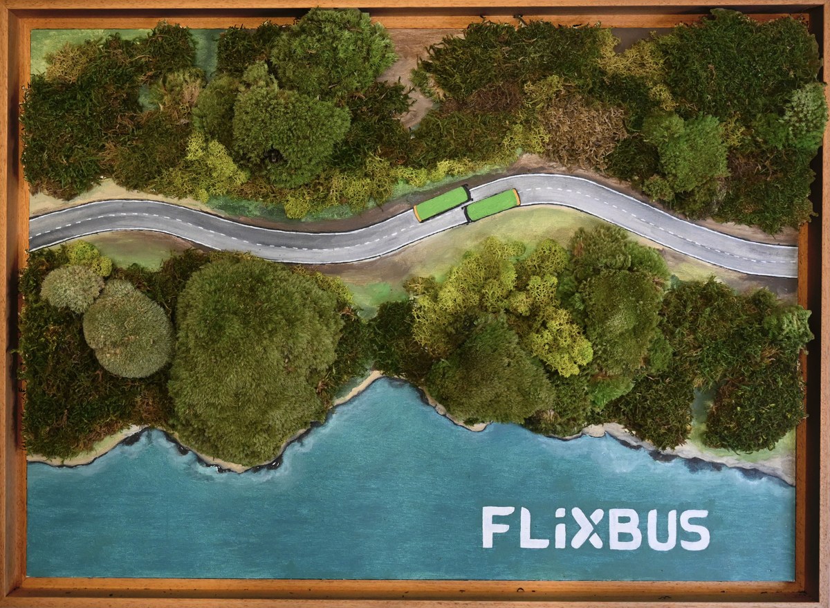 Zelený autobus na klikaté silnici mezi mechovým lesem a modrou vodou s nápisem FlixBus.